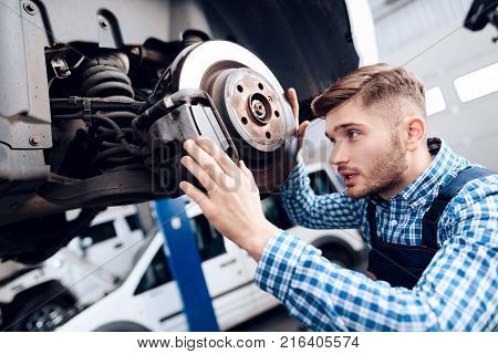 A young man works at a service station. The mechanic is engaged in repairing the car. A young mechanic is repairing the disc brake.
