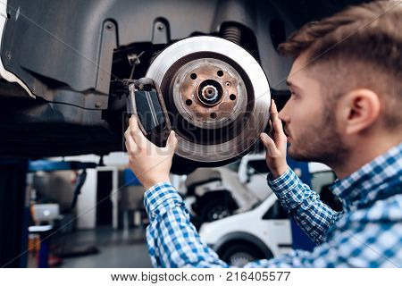 A young man works at a service station. The mechanic is engaged in repairing the car. A young mechanic is repairing the disc brake.