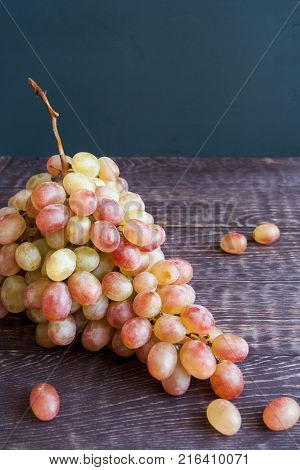 Big tassel of ripe yellow-green-red grapes is lying on dark wooden table and dark gray inhomogeneous background with copy space. Selective focus.