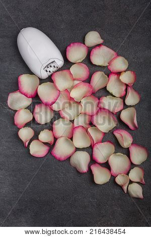Close-up of a female epilator lies near pink rose petals, on a gray background. Depilation.