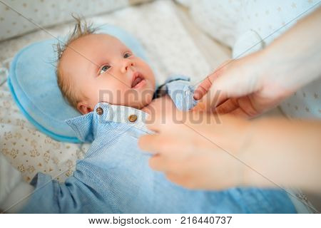 Mom dresses her baby, a newborn lying in a bright room in the crib