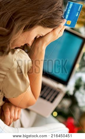 Stressed young woman with credit card and laptop in front of christmas tree