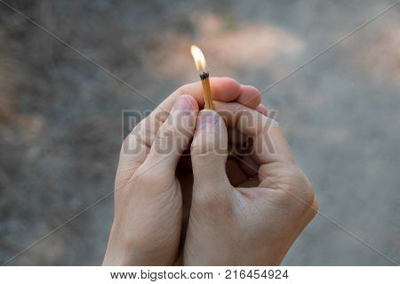 Burning match in hands. The flame from the match pointing to the up. Adult man sand background.