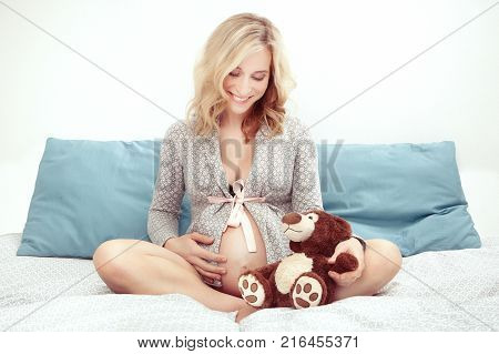 Pregnant young beauty awaiting her newborn while sitting in bed