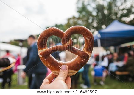 Celebration of the famous German beer festival Oktoberfest. The person holds in his hand a traditional pretzel called Brezel in the background of a blurry people