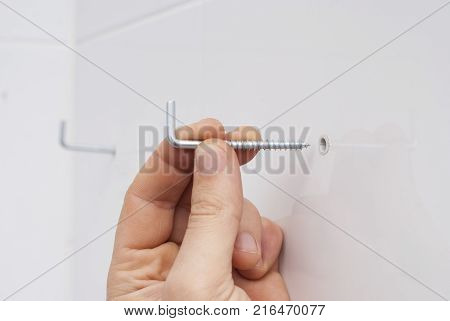 man's hand holds a hook for fixing furniture to the wall