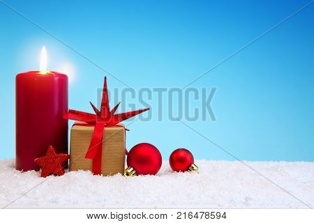 Avent candle and christmas decoration isolated on blue background. Christmas background with snow, candle and gift box .