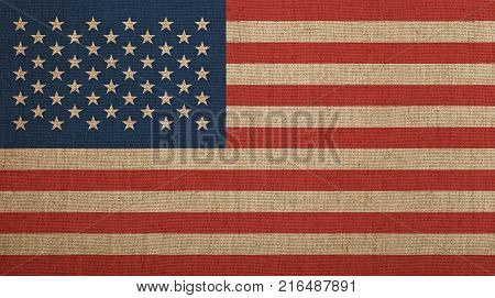 Old grunge vintage dirty faded American US national flag over background of jute linen canvas