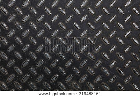 Black painted industrial anti slip embossed metal steel plate with diagonal bumps of diamond pattern texture, background, close up