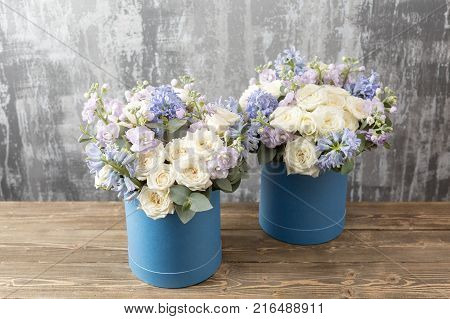 two flower bouquet in a hat box blue. standing on a wooden table. On the background old gray wall art. copy space. blue and white color