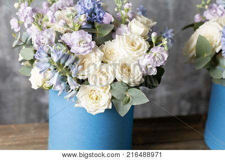 two flower bouquet in a hat box blue. standing on a wooden table. On the background old gray wall art. copy space. blue and white color