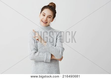 Happiness and enjoy concept. Beautiful adult girl showing at great thing with wide smile. Female enthusiast presenting her preference with finger gesture