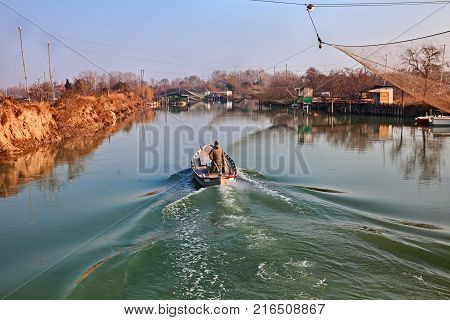 Ravenna, Emilia Romagna, Italy: landscape of the wetland in the nature reserve Po Delta Park, with fisherman in the boat on the river and fishing huts