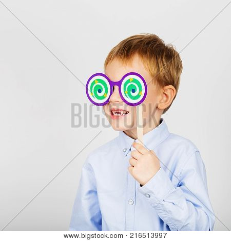 Cute Little School Boy With Funny Paper Glasses Against A White Background. Cheerful Smiling Kid Wit