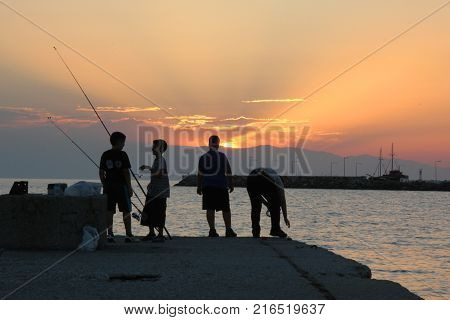 NEA KALLIKRATIA, GREECE - SEPTEMBER 27, 2012: An unidentified group of children is fishing on the pier at sunset.