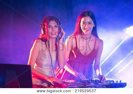 Portrait of active pretty young DJ woman playing music on laser lighting background.