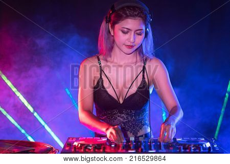 Portrait of active pretty young DJ woman playing music on laser lighting background.