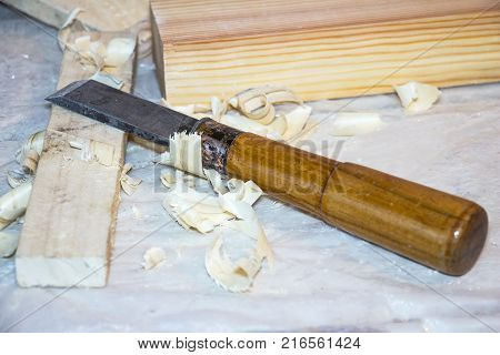 A chisel on the table among the shavings. Nearby there is a wooden bar. Selective focus