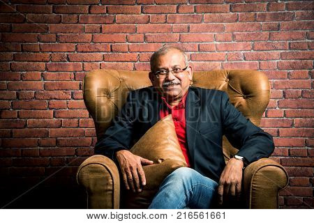 stylish senior indian man in suit sitting on sofa or wing chair. Portrait of Indian or asian millionaire or rich man