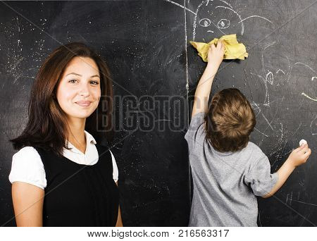 little cute boy in glasses with young real teacher, classroom studying at blackboard school kido close up