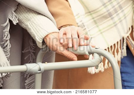 Senior woman with walking frame and young caregiver in park, closeup
