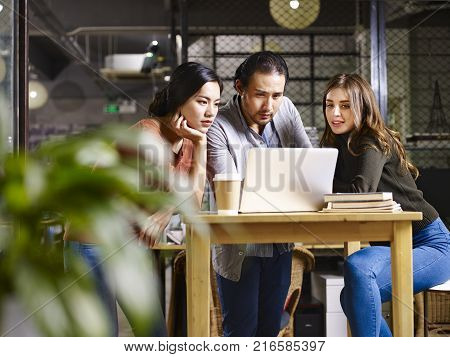 asian and caucasian businesspeople meeting in office discussing business using laptop computer.