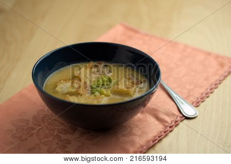 Cauliflower soup into cup, croutons of bread over tablecloth with spoon