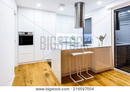 Interior design new modern white kitchen with kitchen appliances. Luxury residential kitchen with sink stove hob and white wooden cupboards and hard wood floor.