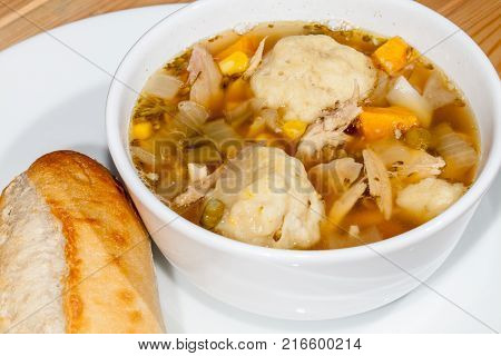Chicken stew and dumplings meal. Hot winter comfort food close up. Chicken and vegetable broth with rustic bread roll from farmhouse kitchen.