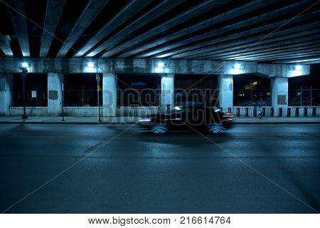 Gritty dark Chicago highway bridge and city street with a passing black car and bicycle stand at night.