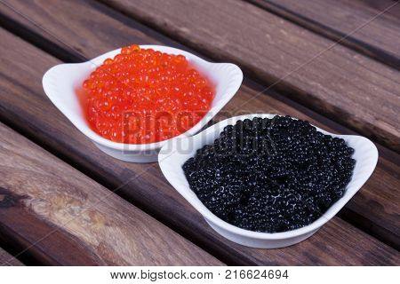 black sturgeon hausen caviar with red salmon caviar in white bowls on wooden background