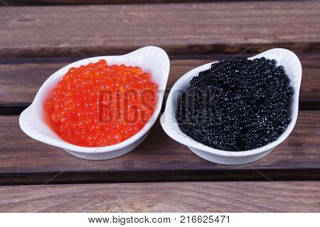 black sturgeon hausen caviar with red salmon caviar in white bowls on wooden background