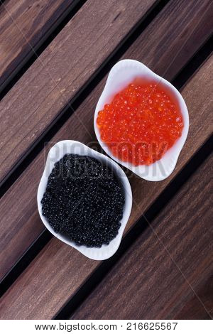 black sturgeon hausen caviar with red salmon caviar in white bowls on wooden background