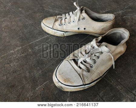 dirty and old white shoes on dirty cement ground