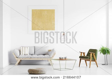 Gold painting above grey sofa in bright living room with armchair at table pouf and fern