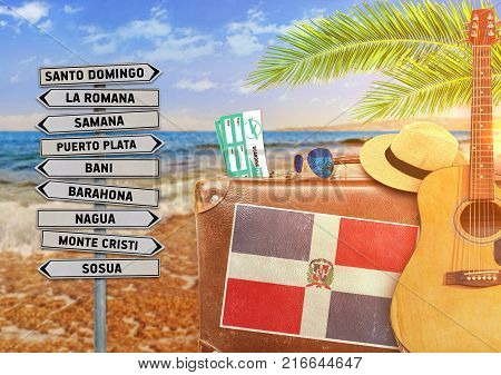 Concept of summer traveling with old suitcase and Dominican Republic town sign with burning sun