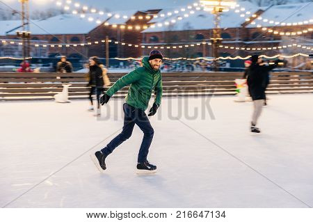 Outdoor Shot Of Unexperienced Male Skater Uses Skate Aid For Go Skating On Ice, Being In Good Mood,