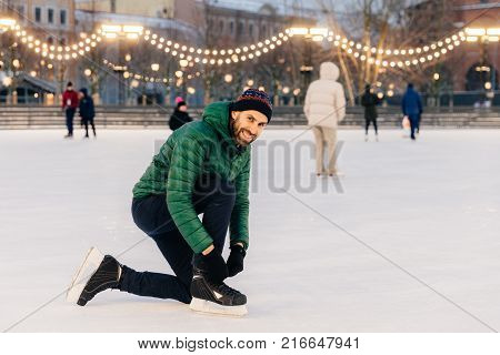 Outdoor Shot Of Unexperienced Male Skater Uses Skate Aid For Go Skating On Ice, Being In Good Mood,