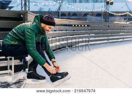 Outdoor Shot Of Unexperienced Male Skater Uses Skate Aid For Go Skating On Ice, Being In Good Mood,
