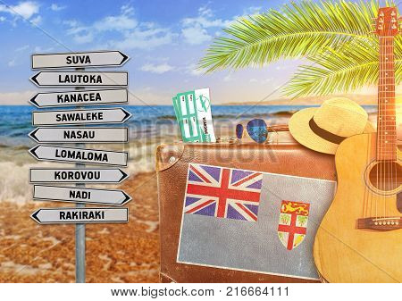Concept of summer traveling with old suitcase and Fiji town sign with burning sun