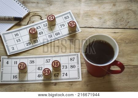 Cards And Chips For Playing Bingo On A Wooden Table. Cup With Coffee