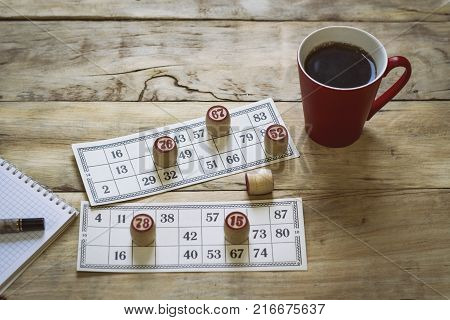 On A Wooden Bingo Table Game, A Cup With A Coffee, A Biscuit And An Orange Slice