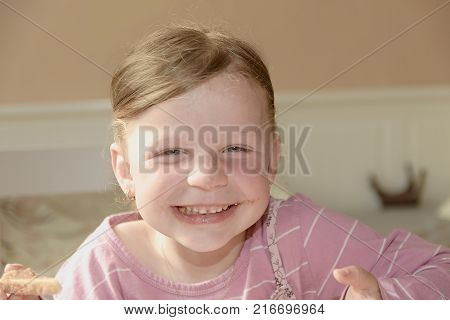 Happy girl has a snack in the kitchen. A cute small girl smiles. A small girl with chocolate cream stains on face. Childhood and fun concep