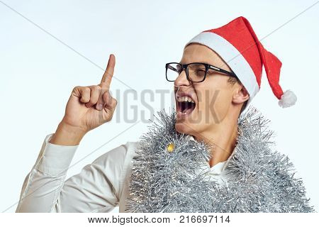 a man in glasses points a finger up, tinsel, a Christmas hat, Christmas, a new year.