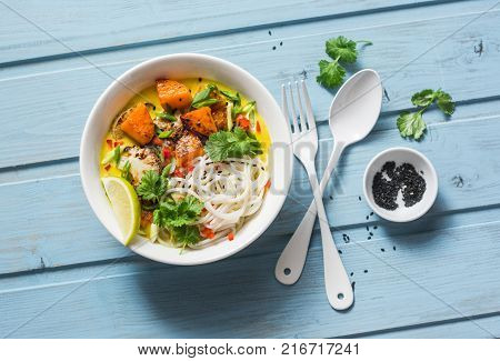 Cauliflower pumpkin curry sauce with rice noodles on wooden blue background top view. Asian style food