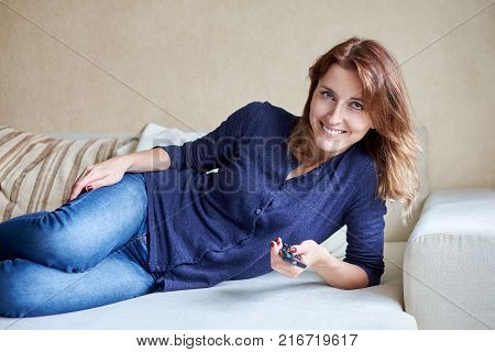 woman relaxing in living room holding remote control and watching television or tv.