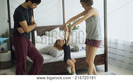 Happy family and little cute daughter dancing and turning around near bed in bedroom at home in the morning