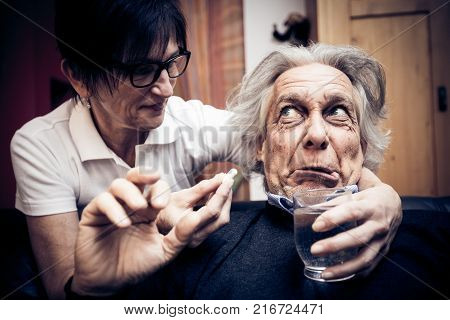 a senior man refusing to take the pills his nurse is trying to give him