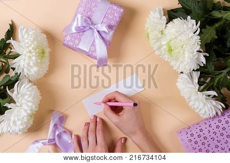 woman hand writing a note with the text thank you on a paper, over beige table and flowers