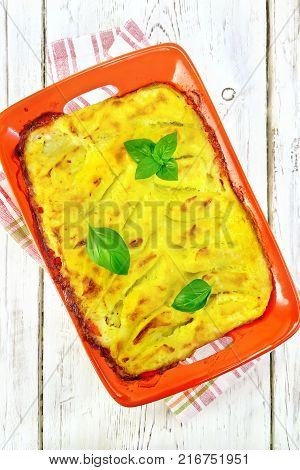 Casserole from mashed potatoes with fish fillets in a brazier on a towel on a wooden plank background